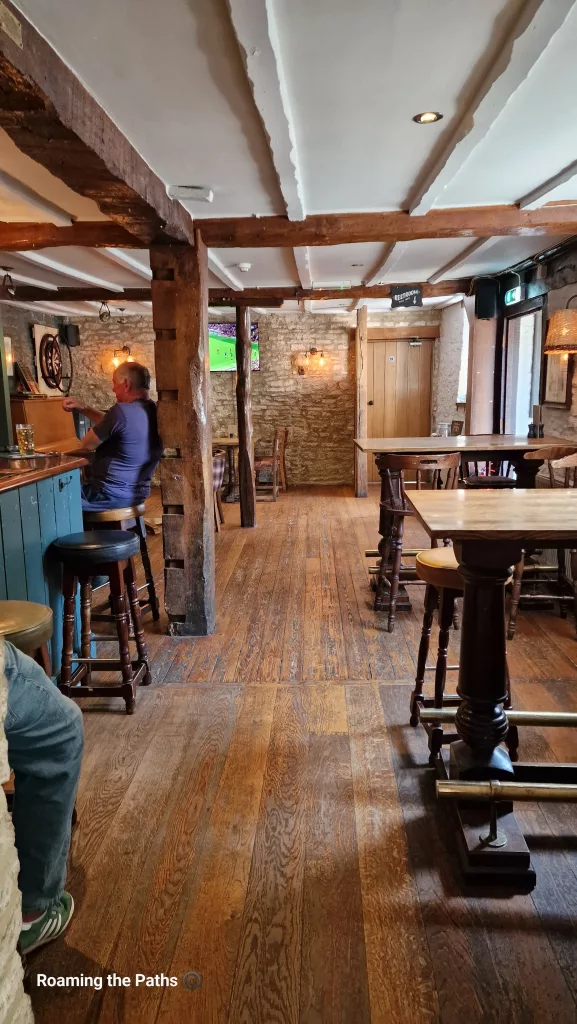 Traditional pub interior with exposed wooden beams, stone walls, wooden floors, and rustic tables at The Bathurst Arms.