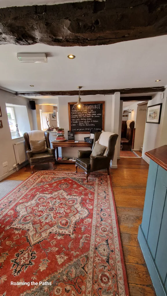 Cosy lounge area inside The Bathurst Arms with leather armchairs, exposed beams, wooden floors, and a large patterned rug in a traditional countryside pub setting.